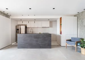A modern, minimalist kitchen featuring a large, dark concrete island and white cabinets.