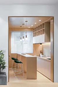 A modern, minimalist kitchen with a wooden island and stools, illuminated by pendant lights hanging from the ceiling.