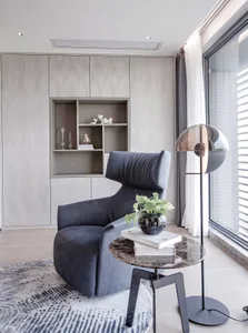 A modern minimalist living room with a dark blue accent chair, a round marble-top side table, and a grey curtain by the windo