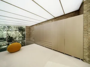 Modern minimalist residential interior with concrete walls and floor, featuring a yellow pouf and large glass windows.