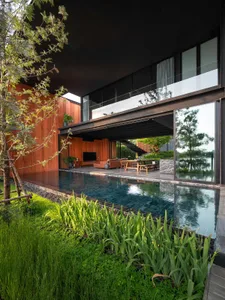 Modern, minimalist residential exterior featuring a large glass wall, wooden accents, and a sleek swimming pool.