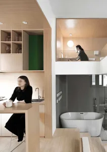 A modern residential interior with wooden elements, featuring a kitchen counter, a floating desk area, and an en-suite bathro