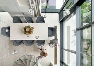Modern dining room with grey furniture and a wooden floor, featuring a round glass table with a floral centerpiece and hangin