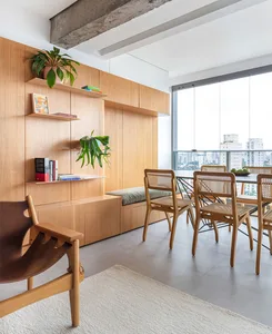 A modern dining room featuring a wooden table and chairs, with a built-in shelf and seating area.