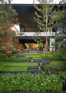 A modern house featuring a concrete exterior with lush landscaping and a water feature.