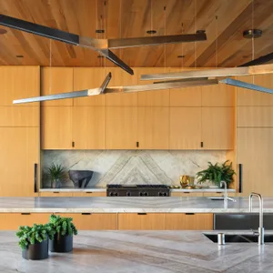 A modern residential kitchen featuring wood cabinets, marble backsplash, and stainless steel appliances and countertops.