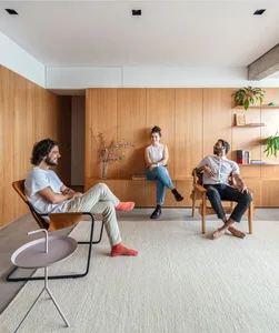 A modern living room with three people sitting on chairs, wooden cabinets, and potted plants.