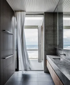 Modern minimalist bathroom featuring a concrete vanity and floor-to-ceiling window offering scenic ocean views.