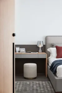 A minimalist bedroom featuring a grey wooden bed frame, soft grey carpet, and a modern wooden desk with a grey cushion.