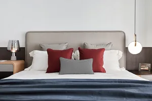A minimalist bedroom with a bed adorned with white, burgundy, and patterned pillows and a textured headboard.