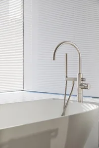 Modern bathroom with a freestanding ceramic bathtub and a sleek, minimalist stainless steel faucet against white vertical bli