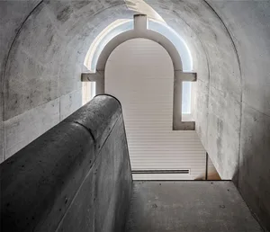 A modern interior space featuring a concrete archway leading to a brightly lit area.
