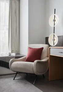 A modern living room with a cozy fabric armchair, a wooden desk, and a contemporary light fixture.