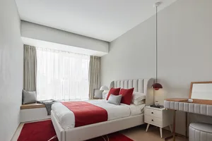 A minimalist bedroom with a white bed, red accents, and a large window with sheer curtains.