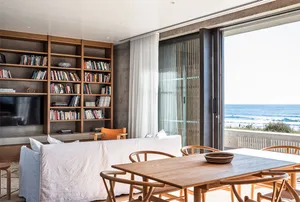 A minimalist living room with a white couch, wooden table, and bookshelf filled with books and decorative items. The room ove