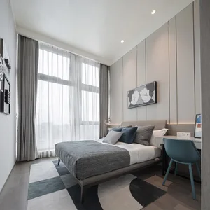A minimalist bedroom with a bed, pillows, and a desk chair, featuring textured fabrics and a window with curtains.