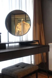 現代簡約梳妝台搭配圓形鏡面與木質飾面，附有椅凳及窗簾窗景。