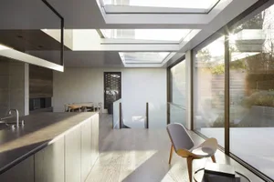 Modern residential interior featuring sleek glass and concrete materials, open-concept space with skylights and large windows