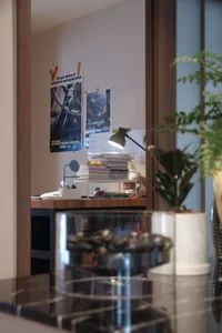 A neatly organized study room with a wooden bookshelf, a stack of books, a small lamp, and a potted plant.