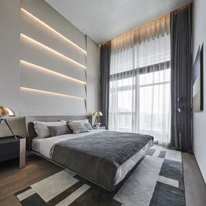 A minimalist bedroom with a gray floating bed, illuminated wall panel, and large windows with dark curtains.