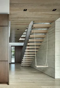 Modern floating stairs with wooden steps and a floating wooden shelf attached to the side wall, illuminated by recessed light