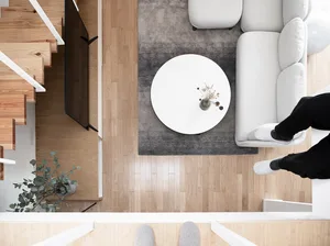 Modern minimalist living room with white furniture, wooden floors, and a circular coffee table.