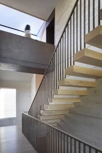 An image showcasing a modern staircase with wooden steps, concrete walls, and a metal railing.