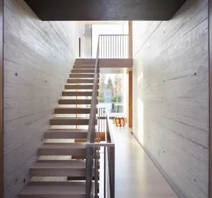 A modern interior staircase with wooden steps and railings, lined with wood-paneled walls.