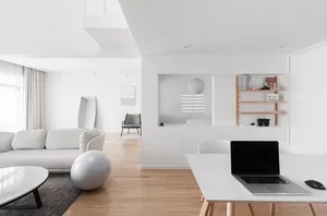 A minimalist modern living room with white furniture, wooden floors, and white walls.