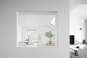 A minimalist space featuring white walls and furniture with a small potted plant and a white dining table with chairs.