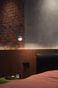 A modern bedroom with brick accent wall, wooden panels, a leather headboard, and metallic bedside lamp.