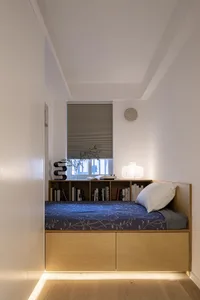 A minimalist bedroom featuring a wooden frame bench with a blue floral bedspread and a white pillow.