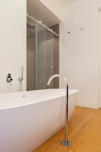 Modern bathroom with white porcelain bathtub, floor-mounted faucet, and glass shower enclosure.