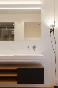 A minimalist bathroom with a sleek white vanity, wood accents, and a large mirror.