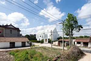 A modern white house with a roof garden, set against a backdrop of greenery and blue sky with clouds.