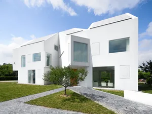 A modern residential building painted entirely in white with large glass windows and solar panels on the roof.