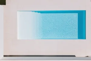 A minimalist outdoor pool with glass walls and a light-colored surrounding area.