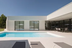 Modern pool house exterior with large glass walls and a concrete patio.