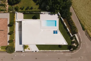 A modern house with a concrete side yard featuring a swimming pool and surrounding greenery.