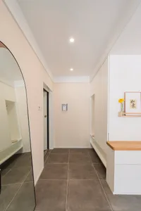 A modern entrance hall featuring ceramic tiles on the floor and walls, with white cabinets and a large curved mirror.