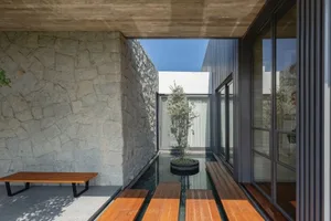 An outdoor residential area featuring stone walls, wooden benches, and a glass walkway with a central tree.