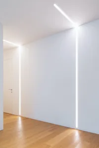 A minimalist white interior design featuring white walls, wood flooring, and linear lighting fixtures.