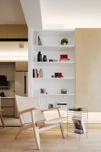 A modern living room featuring a white chair with a woven seat and backrest, white shelves with books and personal items, and