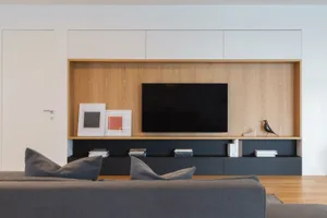 Modern living room featuring wooden shelves, a black television, and gray furniture.