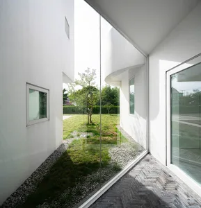 Modern minimalist house exterior with white walls, glass windows, and gravel pathway.