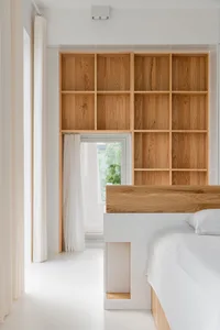 A minimalist modern bedroom with white walls, a wooden bed frame, and white bedding.
