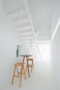 Contemporary minimalist living room with white walls, wooden furniture, and a staircase leading to another level.