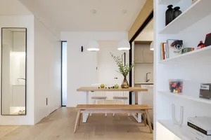 現代簡約廚房，配有木質餐桌、餐椅與長椅。廚房區域採用白色櫥櫃與白色檯面。