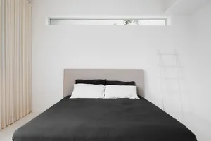 A modern minimalist bedroom featuring a white bed and minimalist decor.