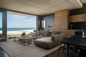 Modern living room featuring a concrete ceiling, wooden furniture, and glass doors overlooking the ocean.